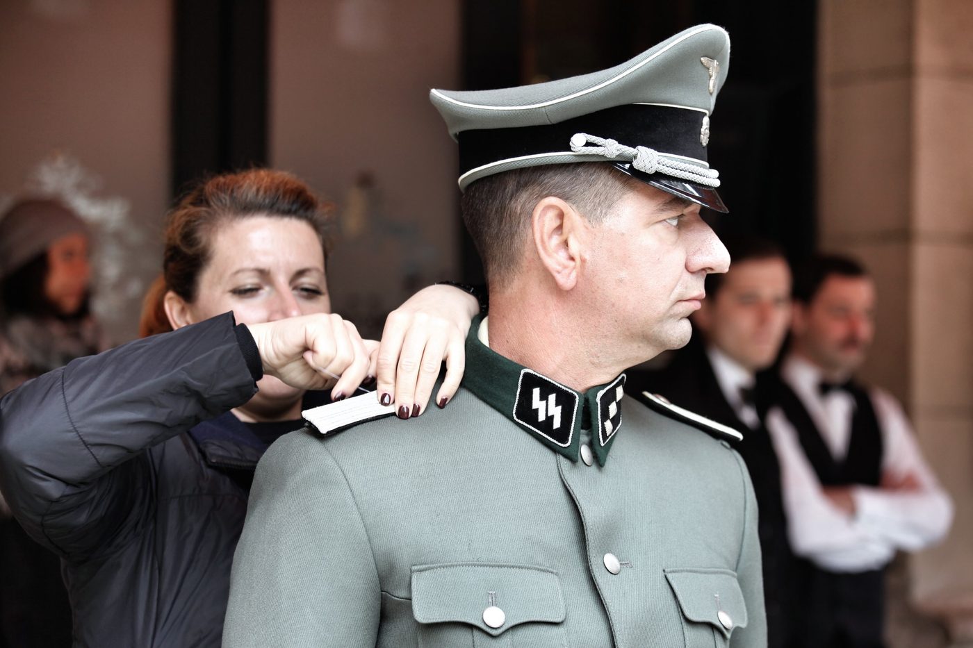 Figurinista ajustando el uniforme de un actor caracterizado de oficial nazi
