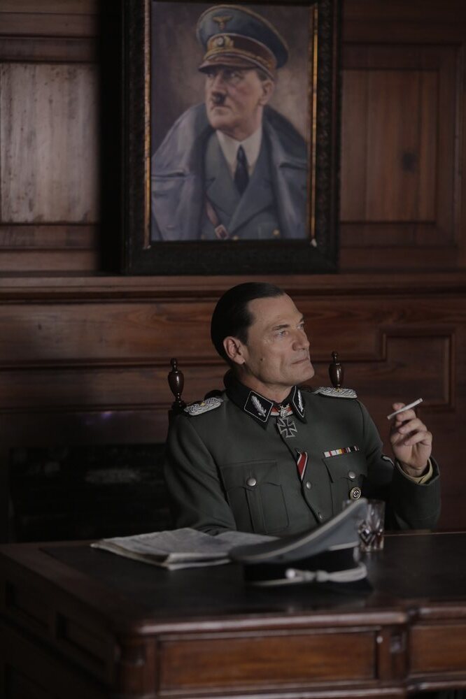 Coronel Maier fumando un cigarrillo bajo un retrato oficial nazi
